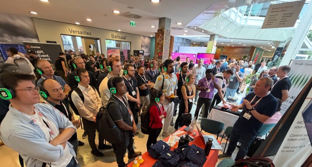 A packed crowd wearing silent-disco headphones watches Danny Dainton give a live demo at the Postman booth during APIdays Munich 2026
